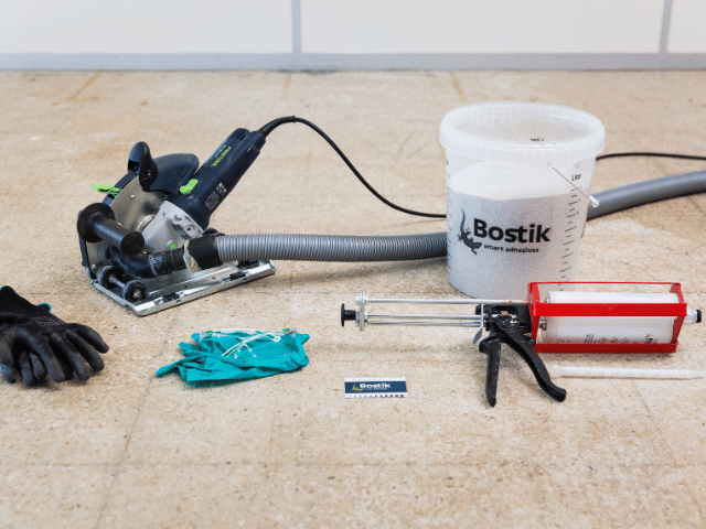 Bostik floor preparation tools including a cutting machine, vacuum, mixing bucket, cartridge gun and protective gloves arranged on a concrete subfloor.