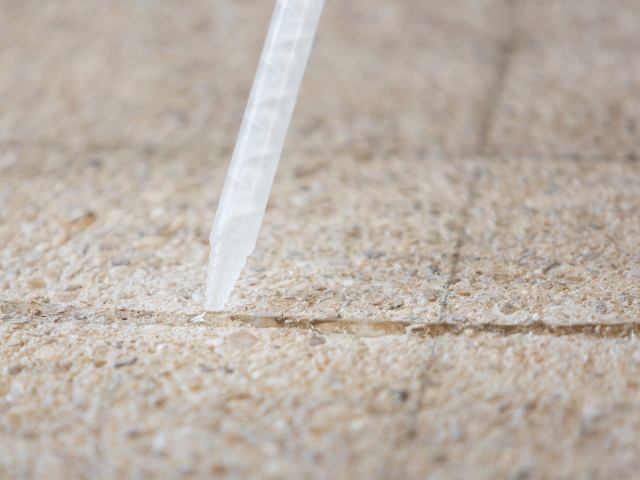 Bostik repair resin being applied with a nozzle into a crack in a concrete floor for precise surface repair.