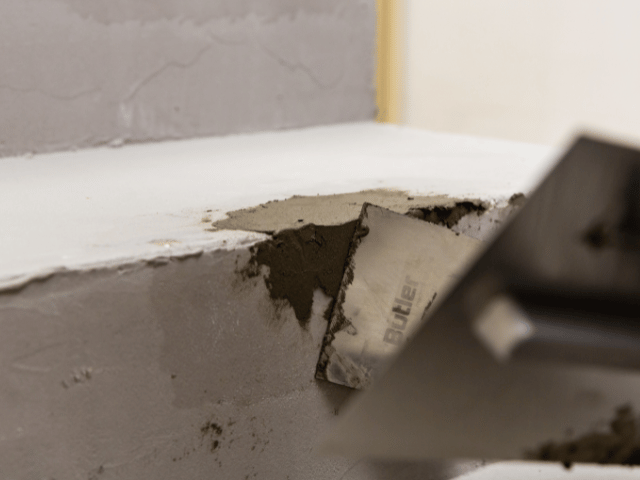 Bostik repair compound being spread with a trowel to smooth and reshape a chipped concrete step corner.