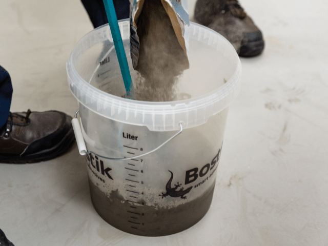 Bostik SL C950 Renoquick powder being poured into a mixing bucket with water to prepare floor levelling compound.