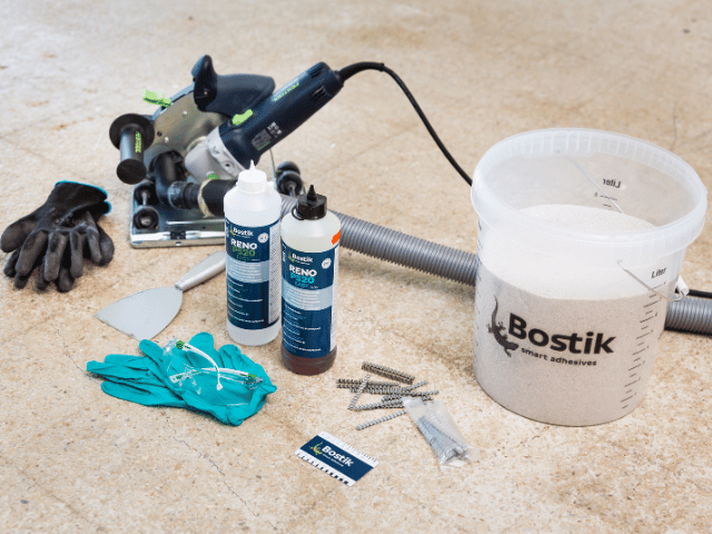 Bostik RENO repair system tools and materials arranged on a concrete floor, including resin bottles, mixing bucket with sand, screws, gloves, and power tools.