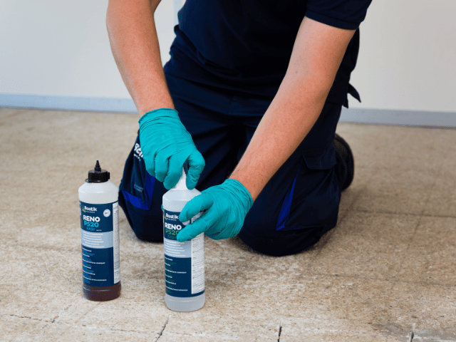 Bostik RENO P520 component bottle being opened by gloved hands on a prepared concrete floor before mixing for repair application.