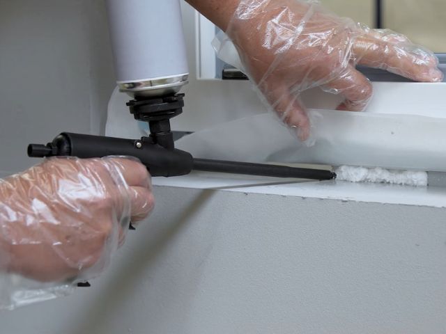Bostik expanding foam being applied with a foam gun into a window frame gap for insulation and sealing.