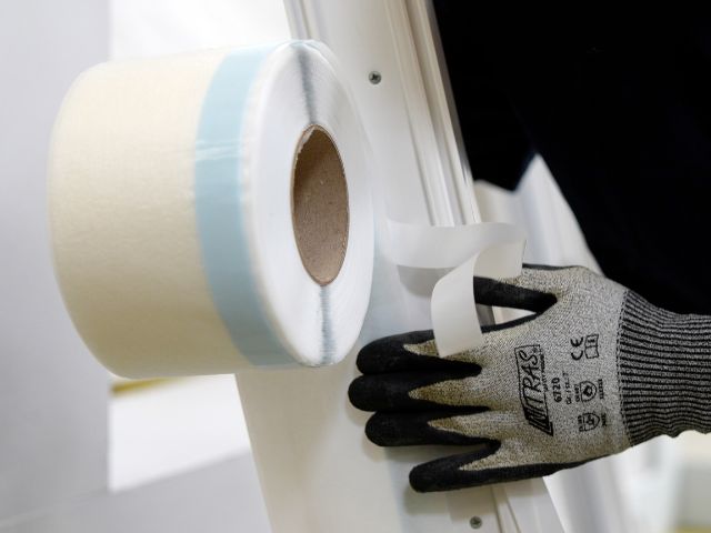 Bostik window insulation tape roll being positioned and applied by hand along a window frame edge for sealing purposes.
