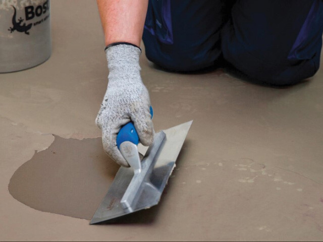 person smoothing out floor surface with a trowel and bostik product
