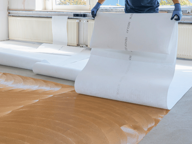 Bostik renovation sheet being laid onto adhesive on a concrete subfloor, smoothing out the surface for flooring installation.