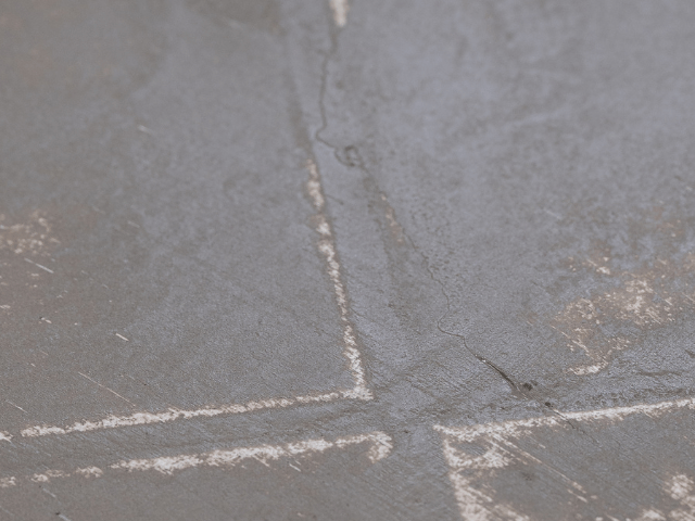 Close-up of a cracked concrete floor with marked intersecting lines, showing surface damage prepared for repair using Bostik floor levelling solutions.