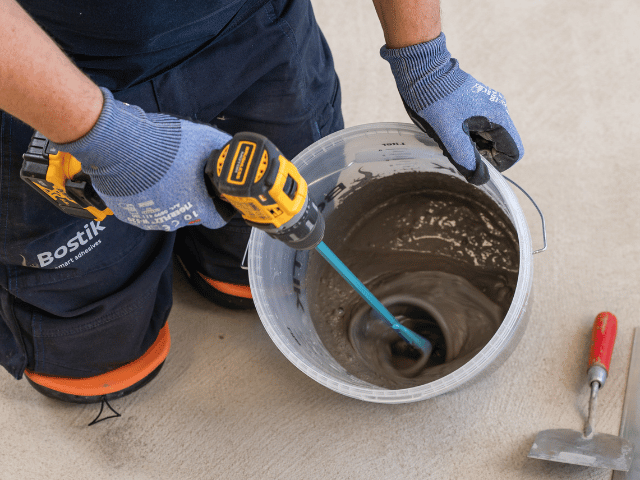 Mixing Bostik floor levelling compound in a bucket using a power drill before application on a concrete surface.