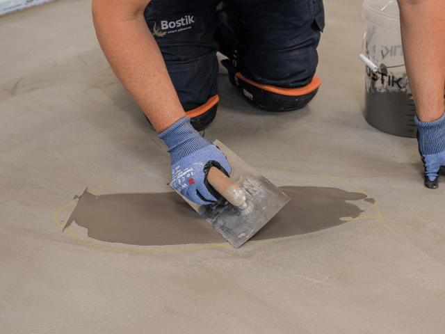 Bostik floor repair compound being spread with a trowel over a marked concrete surface to fill and level a floor area.