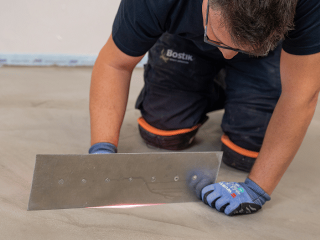 Bostik professional smoothing a floor levelling compound with a large trowel to create an even concrete surface during flooring installation.