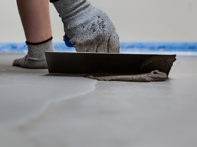 Bostik floor levelling compound being spread with a smoothing trowel across a concrete surface to create an even finish.