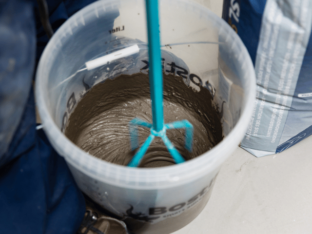 Mixing Bostik floor levelling compound in a bucket using a drill mixer to achieve a smooth and consistent application mixture.