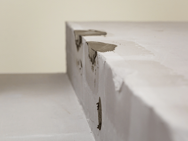 Close-up of a chipped concrete edge filled with Bostik repair compound, showing surface restoration in progress.