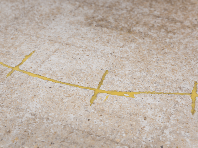 Concrete floor cracks filled with yellow Bostik repair resin, showing sealed joints after injection process.