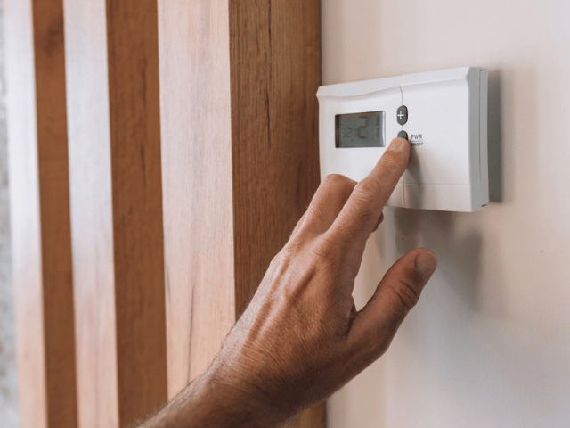 Hand adjusting a wall-mounted thermostat after completing concrete floor repair using Bostik RENO system.