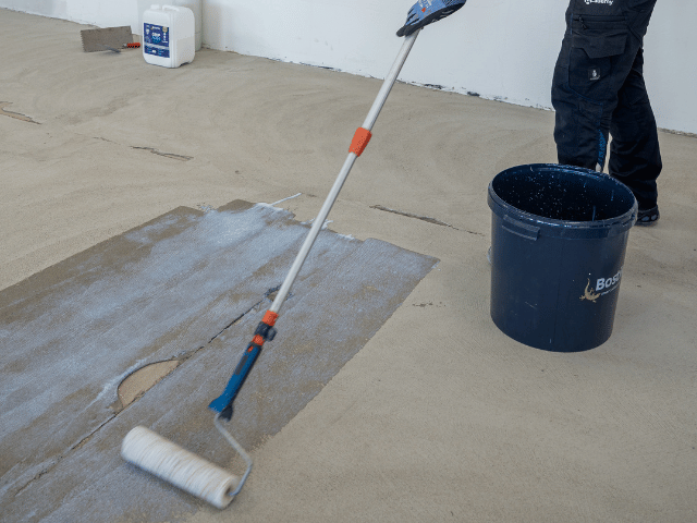 Bostik primer being applied with a roller onto a concrete floor to prepare the surface for further flooring installation.