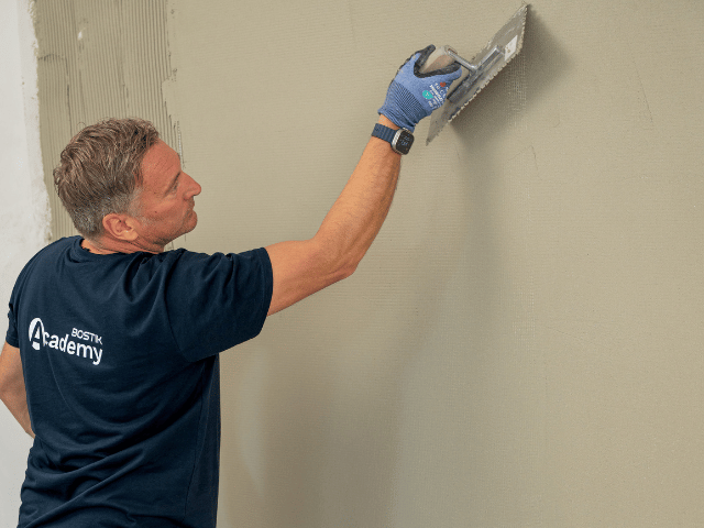 Bostik professional smoothing a levelling compound on a wall surface with a trowel to create a clean and even finish during renovation work.