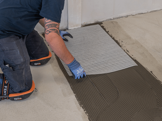 Bostik reinforcement underlay being placed into freshly applied adhesive on a concrete subfloor during flooring installation.