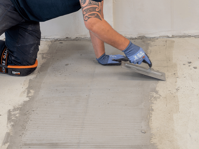 Bostik levelling compound being smoothed with a trowel over a prepared concrete floor to create an even surface.