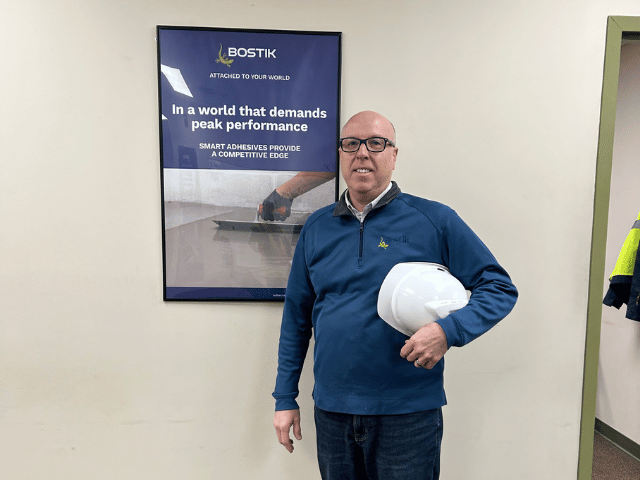 A man standing in front of a picture frame, holding a safety helmet. 