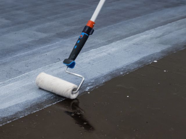 Paint roller applying a Bostik waterproofing layer onto a textured surface, creating a uniform protective finish.