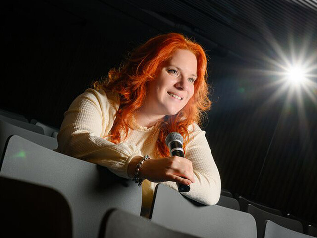 Cecilia leaning over auditorium seats with microphone in hand